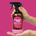 Hand holding a 'frankly real' spray bottle against a pink background