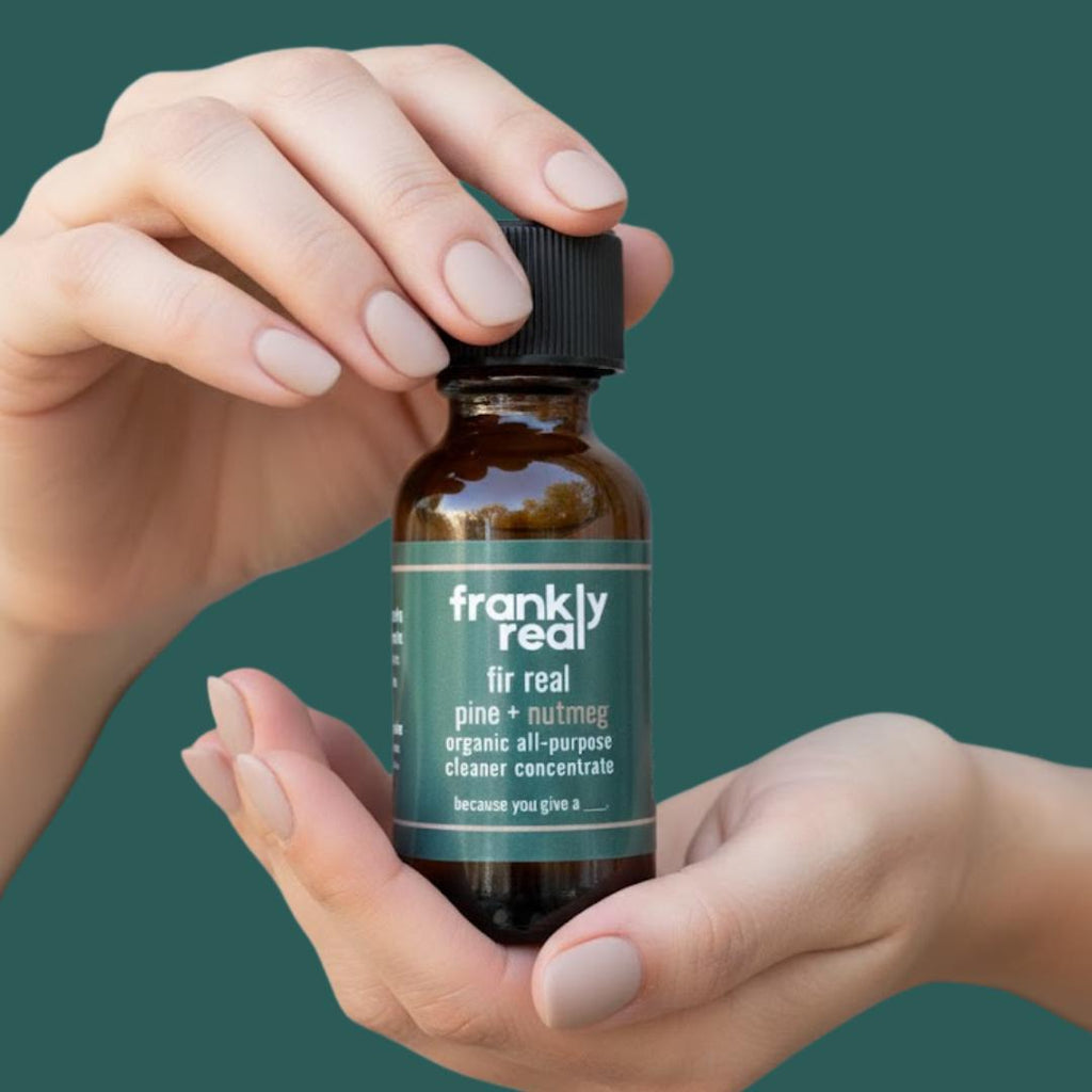 Hand holding a bottle of 'frankly real' all-purpose cleaner concentrate against a green background